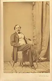 Photographie de Félix Milliet, posant assis sur une chaise, les jambes croisées.