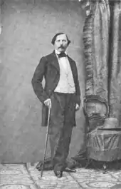 Photographie en pieds de Félix Milliet, posant debout, en costume, une canne à la main.