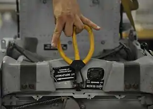 Un technicien montre la manœuvre qu'effectue un pilote de F-16 lorsqu'il doit s'éjecter, en saisissant la poignée entre ses jambes.