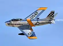 Photographie couleur d'un avion North American F-86 Sabre en vol se détachant sur un ciel bleu.
