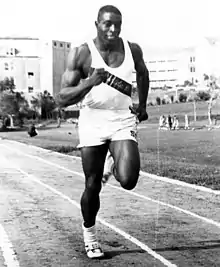 Photo en noir et blanc d'un athlète, de face, courant sur une piste en cendrée.