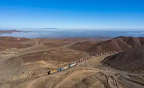 Train de minerai Ferrocarril depuis la mine de San Cristóbal en Bolivie jusqu'à Mejillones au Chili. Il est motorisé en particulier par des Locomotora EMD GT22CU (es). L'horizon se perd dans un brouillard côtier. Juillet 2019.