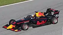 Photographie d'une monoplace de F3 aux couleurs de Red Bull bleu foncé rouge et jaune, vue de trois-quarts droit, d'en haut, dans son ensemble, sur une piste sèche.