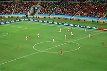 Photo d'un match de football entre une équipe jouant en blanc et l'autre en rouge vu depuis les tribunes