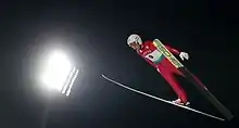 Un sauteur à ski en plein saut vu légèrement de côté.