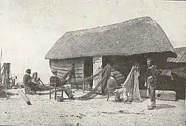 Réparation des Filets, sur les galets d'Étretat au pied d'une caloge, bateau de pêche couvert d'un toit, transformé en appentis pour ranger le matériel.