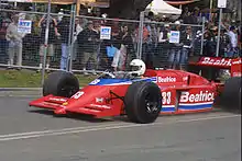 Photographie d'une monoplace de Formule 1 rouge, vue de trois-quarts, devant des spectateurs.