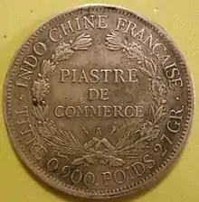 Photographie d'une pièce de monnaie ancienne, portant les mentions « Indochine française » et « Piastre de commerce ».