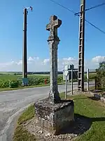 Une croix en pierre, sans ornement remarquable, au bord d'une route.