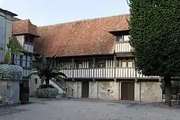 Photographie en couleurs d'une maison à pans de bois au fond d'une cour.