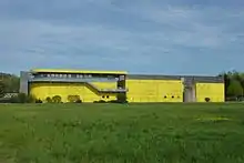 Photographie d'un bâtiment moderne jaune dans un champ.