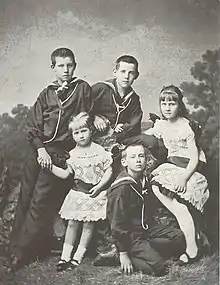 Photo de groupe en noir et blanc qui montre cinq enfants et adolescents. Les trois garçons portent un uniforme de marin, les deux filles portent une robe blanche.
