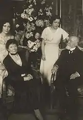 Photo sépia de quatre individus : au premier plan, assis chacun sur un fauteuil, une femme aux cheveux foncés vêtue d'une robe noire, et un homme chauve à la barbe blanche, également habillé en noir, avec cravate et chemise blanche ; à l’arrière-plan se tiennent debout deux femmes plus jeunes, aux cheveux foncés et portant une robe claire