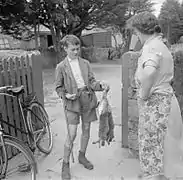 Photo en noir et blanc d'un jeune garçon avec un fusil rapportant deux lapins morts à sa mère
