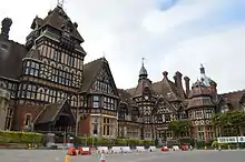 Photo en couleurs d'un vaste château de style Tudor, orné de diverses toitures et clochetons en tuiles rouges.