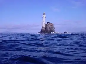 Îlot sur lequel s'élève un phare. Dans le lointain, on aperçoit la côte d'Irlande.