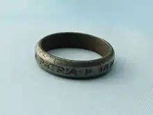 Photographie d'une bague gravée sur l’extérieur en lettres capitales, posée à plat sur un fond bleu