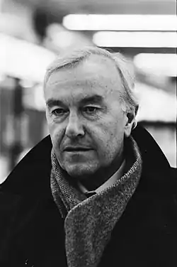 Photographie en noir et blanc d'un homme aux cheveux blancs, avec un manteau noir.