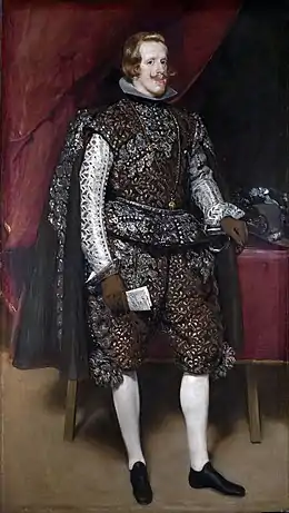 Le roi d'Espagne debout, vêtu de noir et d'argent dans une scène d'intérieur du palais.