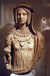 Buste avec bras en terre-cuite d'une femme aux cheveux longs, portant une coiffe et plusieurs colliers en ornement.