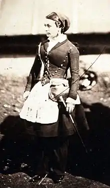 Photographie d'une femme portant un uniforme sombre composé d'un corset et d'une jupe par dessus un pantalon