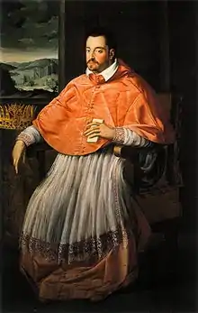 Un homme en tenue de cardinal est assis dans un fauteuil, et tient un papier à la main.