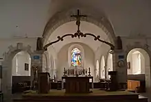 L'intérieur d'une église. Au centre se trouve l'autel, surmonté d'un crucifix. À l'arrière plan, le chœur.