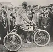 Photo d'un homme en tenue de ville sur un vélo portant un numéro à l'occasion d'une course.