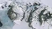 Vue aérienne de massifs montagneux aux sommets enneigés mais entourés de vallées dépourvues de neige présentant quelques petits lacs.