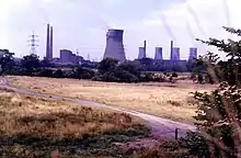 Photo d'un champ d'herbe jaunie avec de grandes cheminées crachant de la fumée et des lignes à haute tension à l'horizon