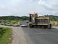 Loco n° 21 traversant Nadi Back Road dans les champs de canne à sucre avec quelques wagons vides. La ligne principale est parallèle à la route sur la gauche.