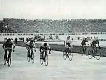 Photo de six coureurs cyclistes roulant presque de front sur un vélodrome.