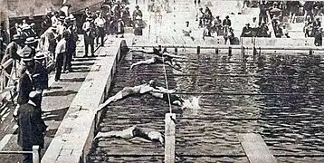 Photo de plusieurs hommes sautant d'une plongeoir de natation et touchant la surface de l'eau.