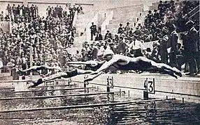 Photo de plusieurs hommes sautant d'une plongeoir de natation et touchant la surface de l'eau.