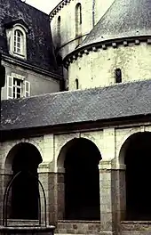 Photographie d'arcades d'une galerie d'un cloître, avec l'église derrière