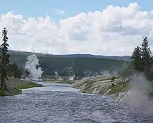 Photographie de la rivière Firehole et d'un geyser en éruption en arrière-plan.