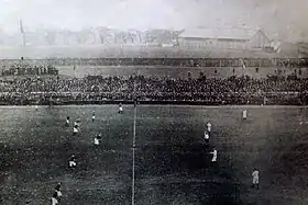 Photographie en noir et blanc de très basse résolution montrant les joueurs sur le terrain du point de vue des tribunes.