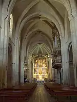 Photographie couleur d'une nef d'église se terminant par un retable.
