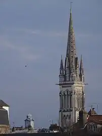 Photographie en couleurs de la flèche d'une église dépassant au-dessus des toits.