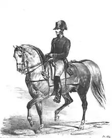 Un militaire en uniforme et bicorne monte un cheval gris rassemblé en bride.