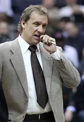 Flip Saunders, en costume, mordant dans un crayon qu'il tient de la main gauche.