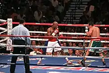 Deux boxeurs en garde, sur un ring, se font face sous le yeux d'un arbitre officiel.