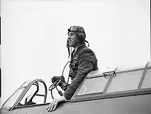 Photographie en noir et blanc d'un homme portant un casque, debout dans le cockpit d'un avion