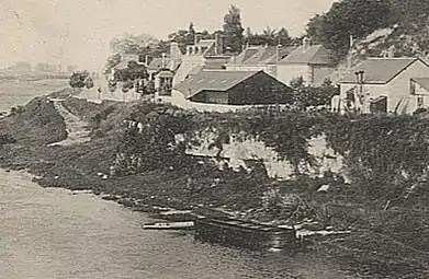 Photographie en noir et blanc de pavillons en bordure de fleuve.