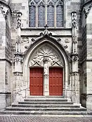 Photographie en couleurs de la façade d'un bâtiment religieux pourvu de ses bas-reliefs, de ses statues et de ses vitraux.