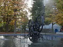 Une fontaine en métal devant un paysage automnal