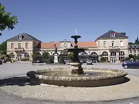 Photographie en couleurs, représentant une place publique et une fontaine.