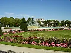  Photographie d'un jardin public, ses massifs de fleur et sa grande fontaine.