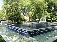 Photographie en couleurs d'une fontaine dans un espace vert public.