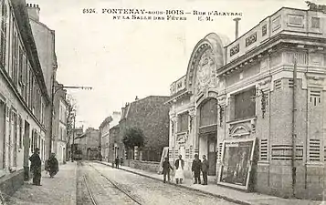 Carte postale noire et blanche. Rue bordée d'immeubles d'un étage, en regard bâtiment avec fronton.